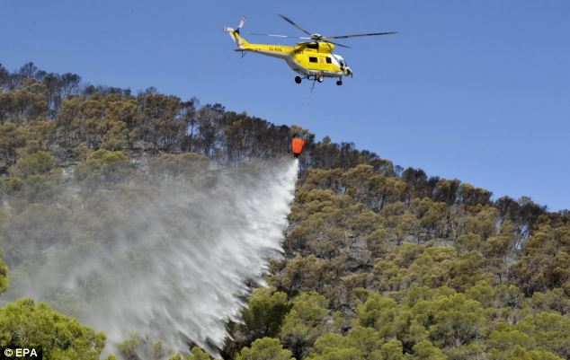 Night and day,
        air and land: A rescue services helicopter bombs the fire front
        with water. Despite the best efforts, the fire is still
        threatening homes and resorts on the popular holiday island
